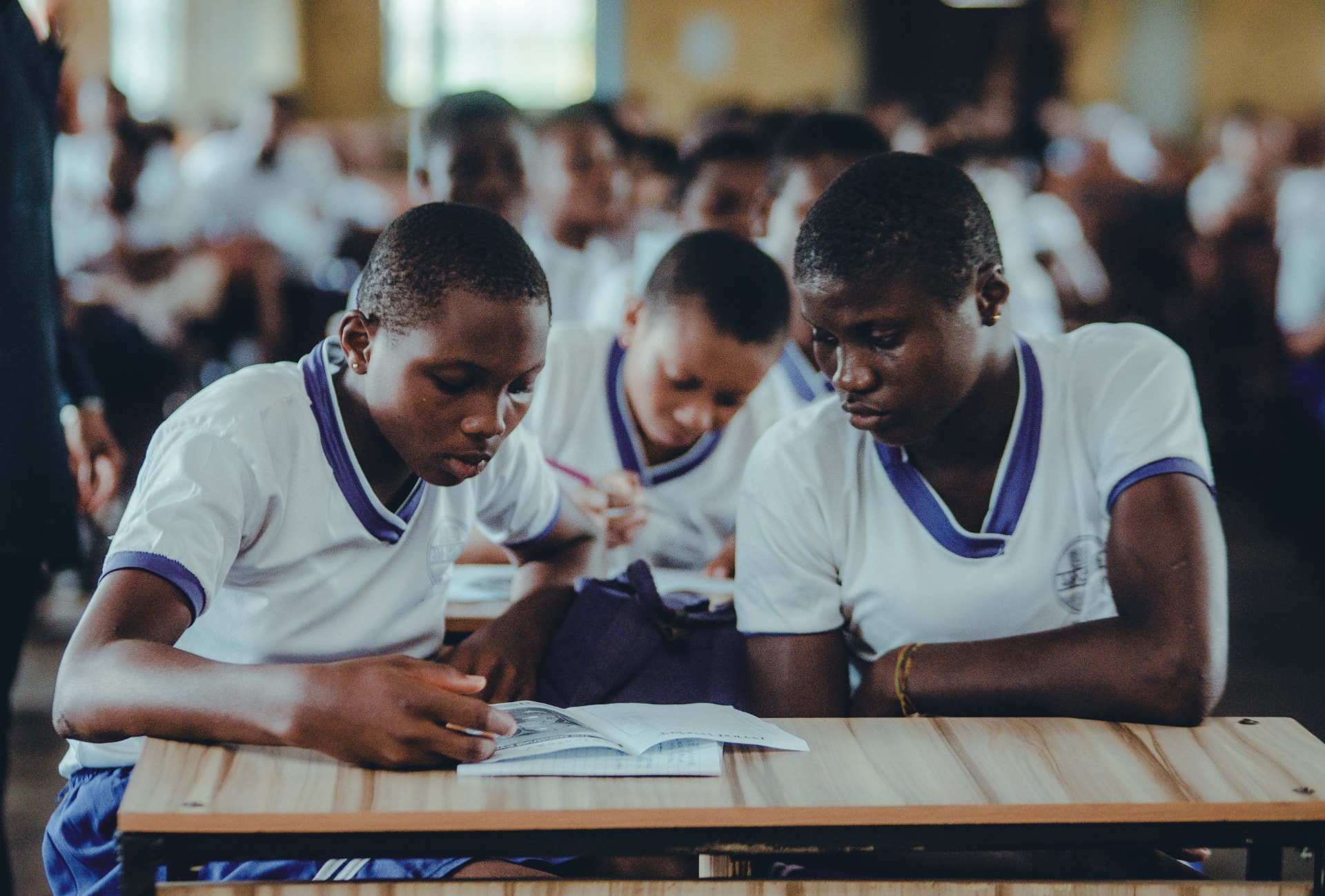 Two learners reading a shared exercise book at a classroom desk