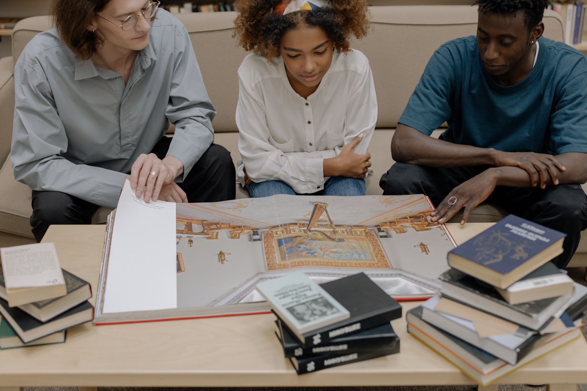 Three readers looking through large illustrated books at a low table